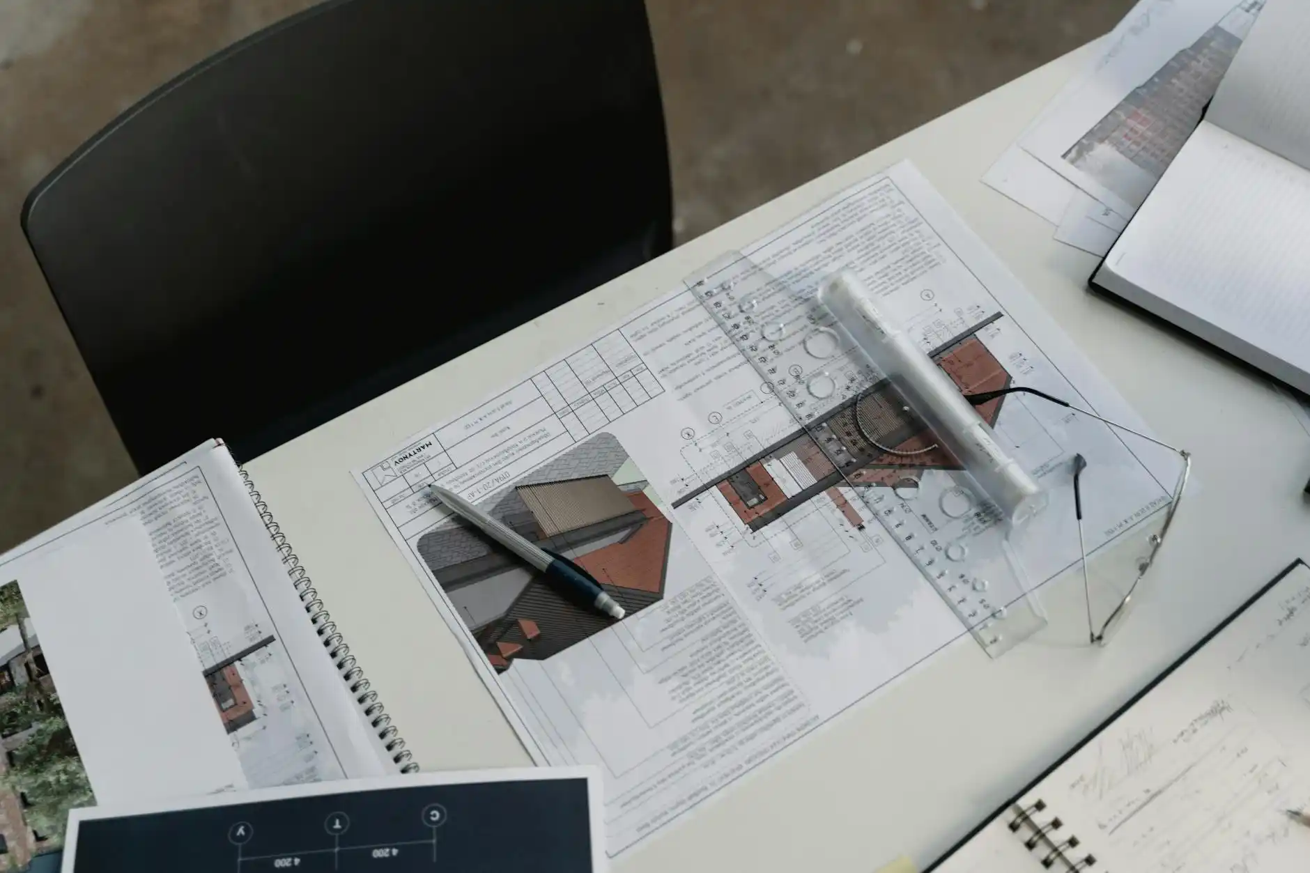 detailed architectural construction drawing set spread across a drafting desk with scale ruler, material samples, and a laptop displaying a 3D custom home model