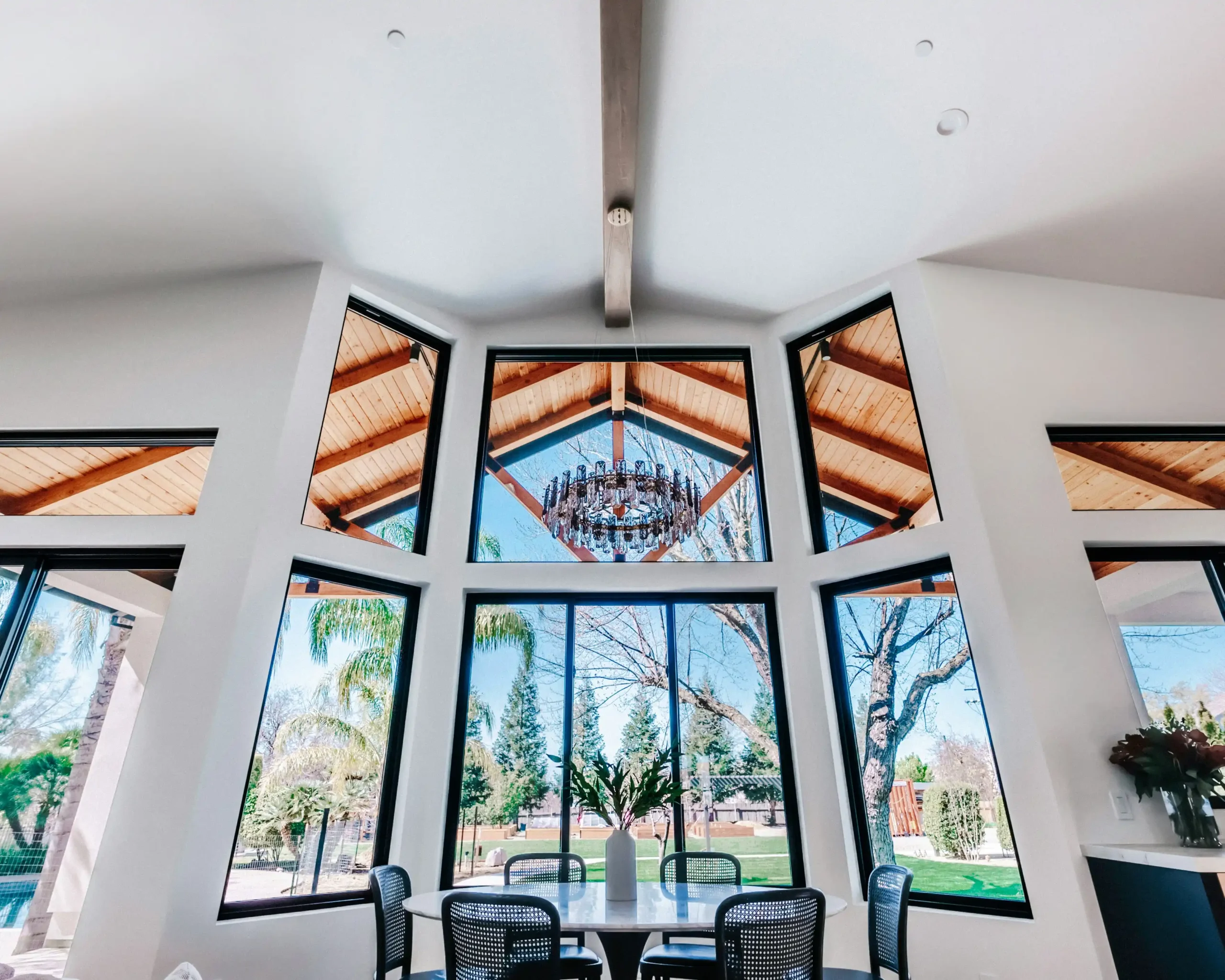 custom luxury home exterior on a sloped wooded lot, black-framed windows, mixed stone and cedar facade, landscaped entry path, and warm sunset lighting