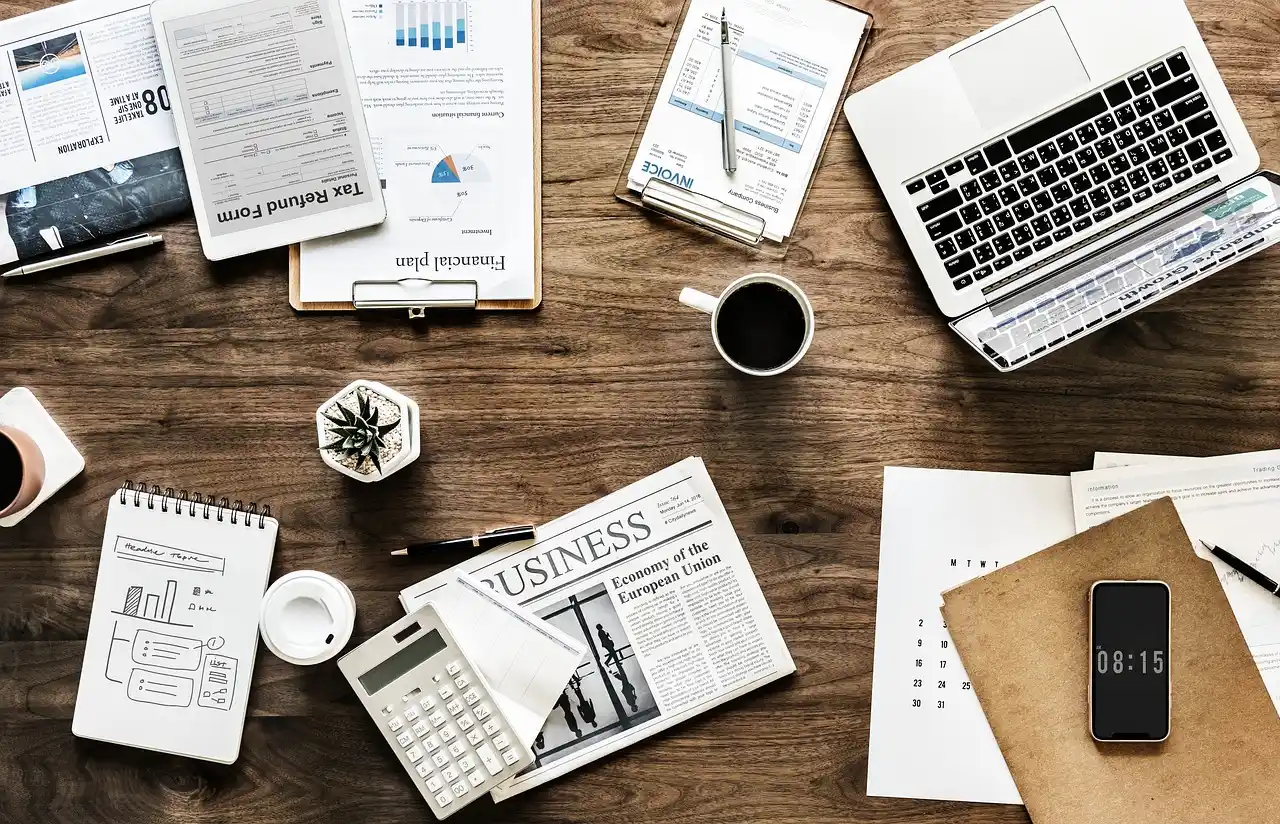 side-by-side renovation estimates on a wooden desk, highlighted line items for kitchen, bathroom, flooring, and roofing, calculator and coffee mug beside blueprint plans