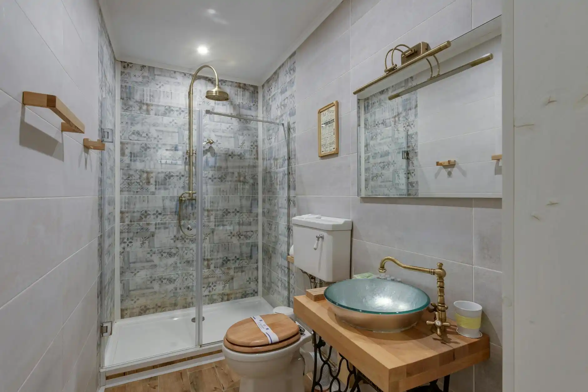 close-up collage of mid-range bathroom materials including oak vanity cabinet, white quartz slab, stacked porcelain wall tile, hex floor tile, brushed brass faucet, and clear gl...