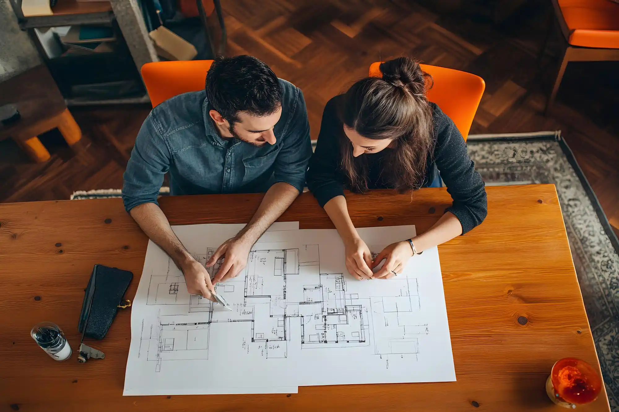 architect and homeowners reviewing custom home plans at a wood table with Seattle neighborhood map, material samples, and laptop showing 3D rendering