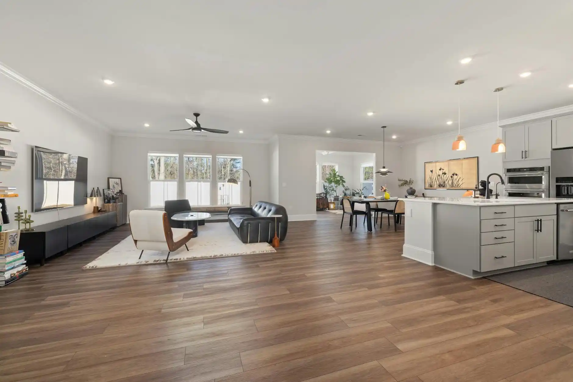 bright open-concept kitchen and living area with wide plank white oak floors, full-height oak cabinetry, waterfall quartz island, and matte black window frames