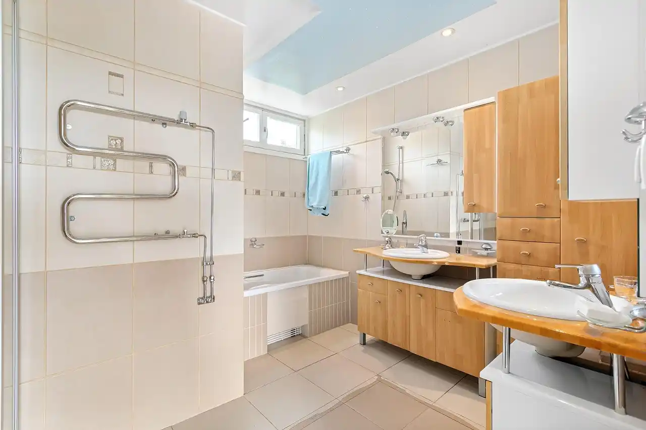 spa-inspired primary bathroom with large format porcelain tile, floating walnut vanity, brushed brass faucets, frameless glass shower, and soft natural daylight