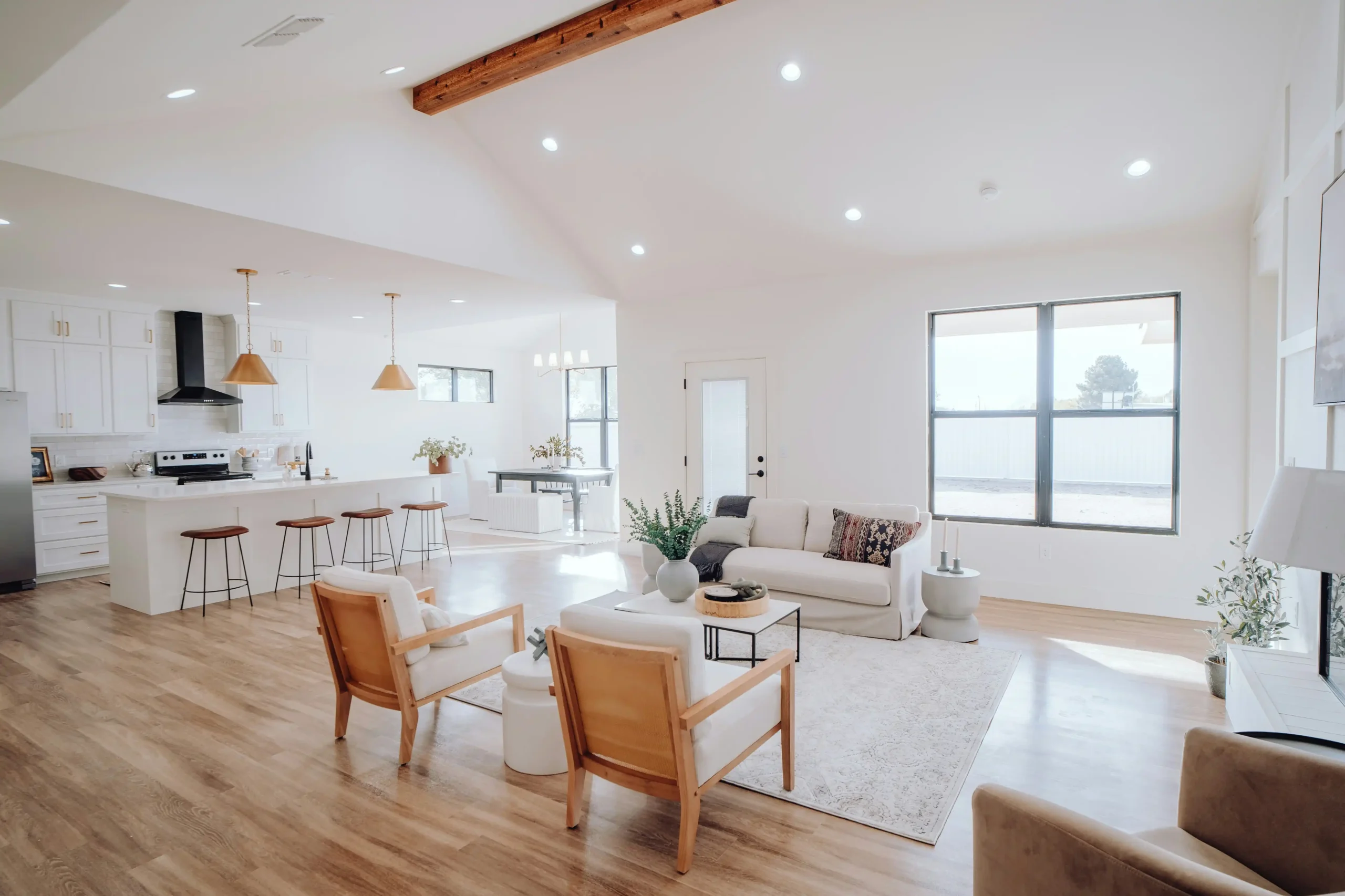 contractor in a remodeled living room pointing to a printed scope of work with flooring samples, paint swatches, and cabinet finish selections spread across a kitchen island