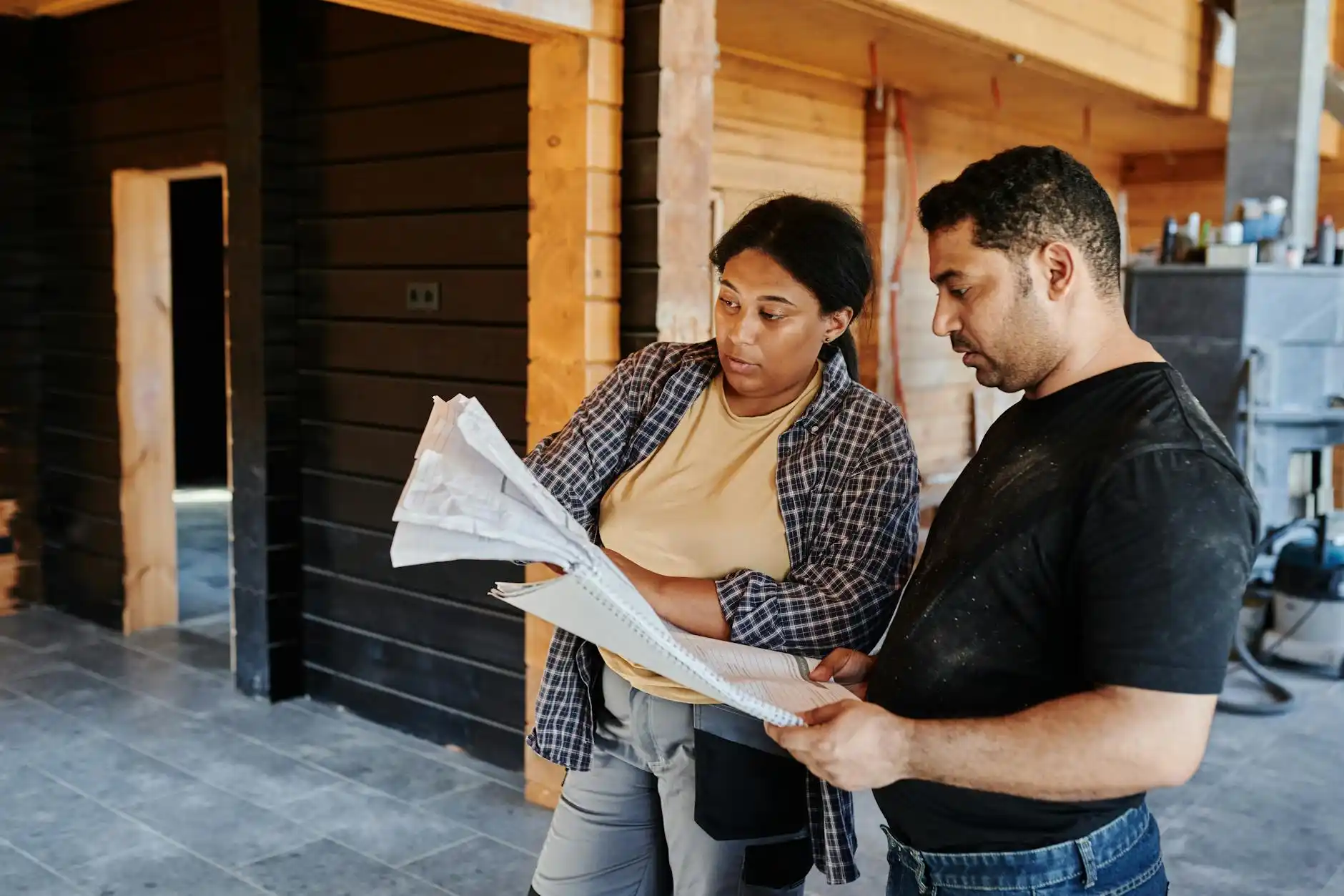 custom home construction site at golden hour with framed two-story house, workers reviewing plans, cranes in background, and a luxury neighborhood under development