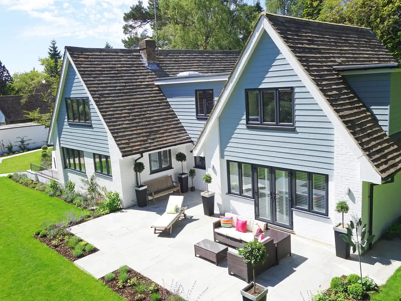 happy homeowners in front of newly completed modern custom house with black-framed windows, warm wood accents, and landscaped front walk at golden hour