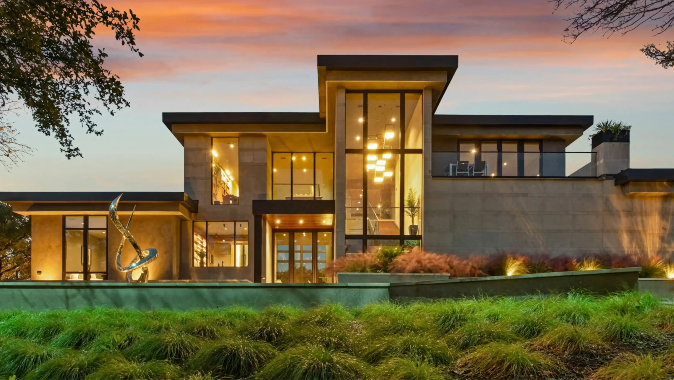 newly built contemporary custom home exterior at dusk with warm interior glow, smartphone-controlled lighting visible through large black-framed windows, landscaped front entry ...