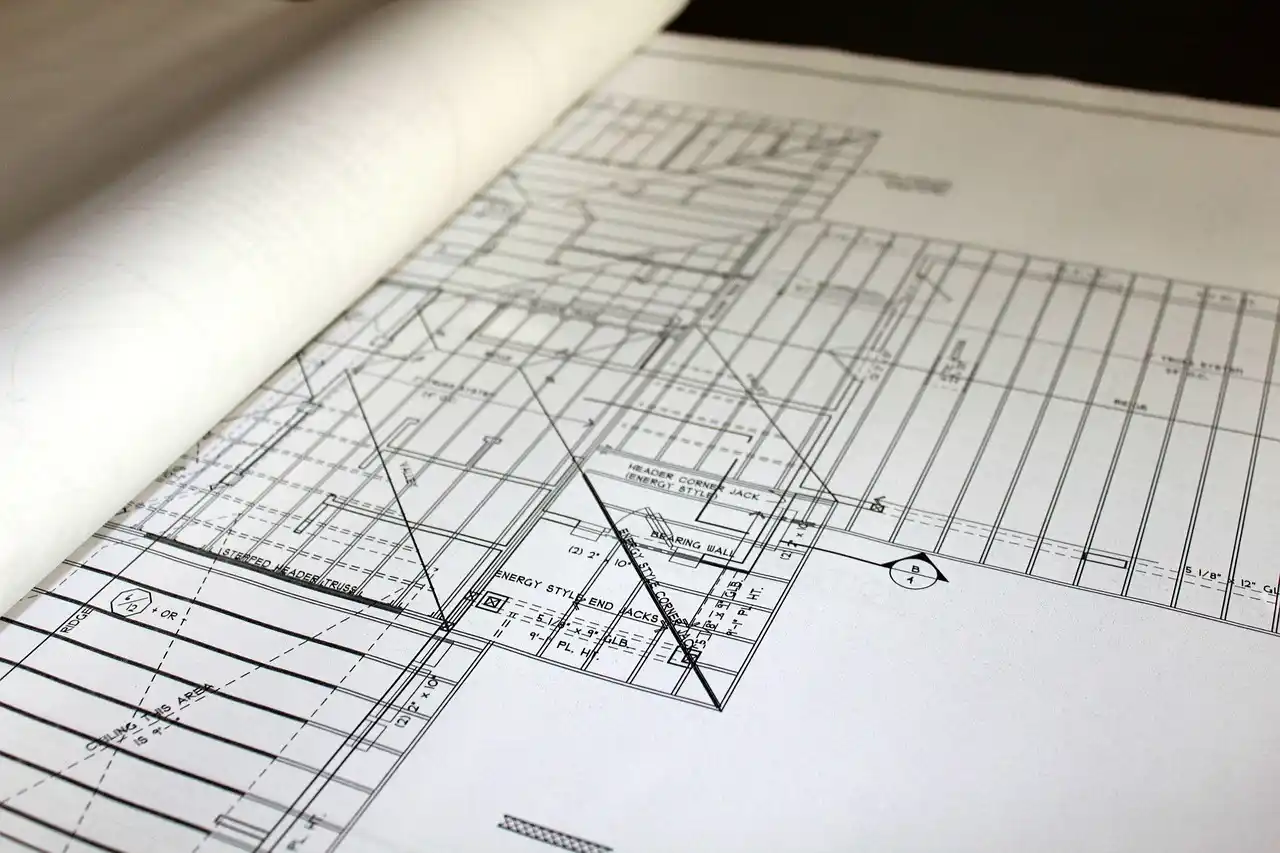 licensed contractor reviewing bathroom permit plans beside open wall framing with visible plumbing lines, electrical boxes, and ventilation ductwork