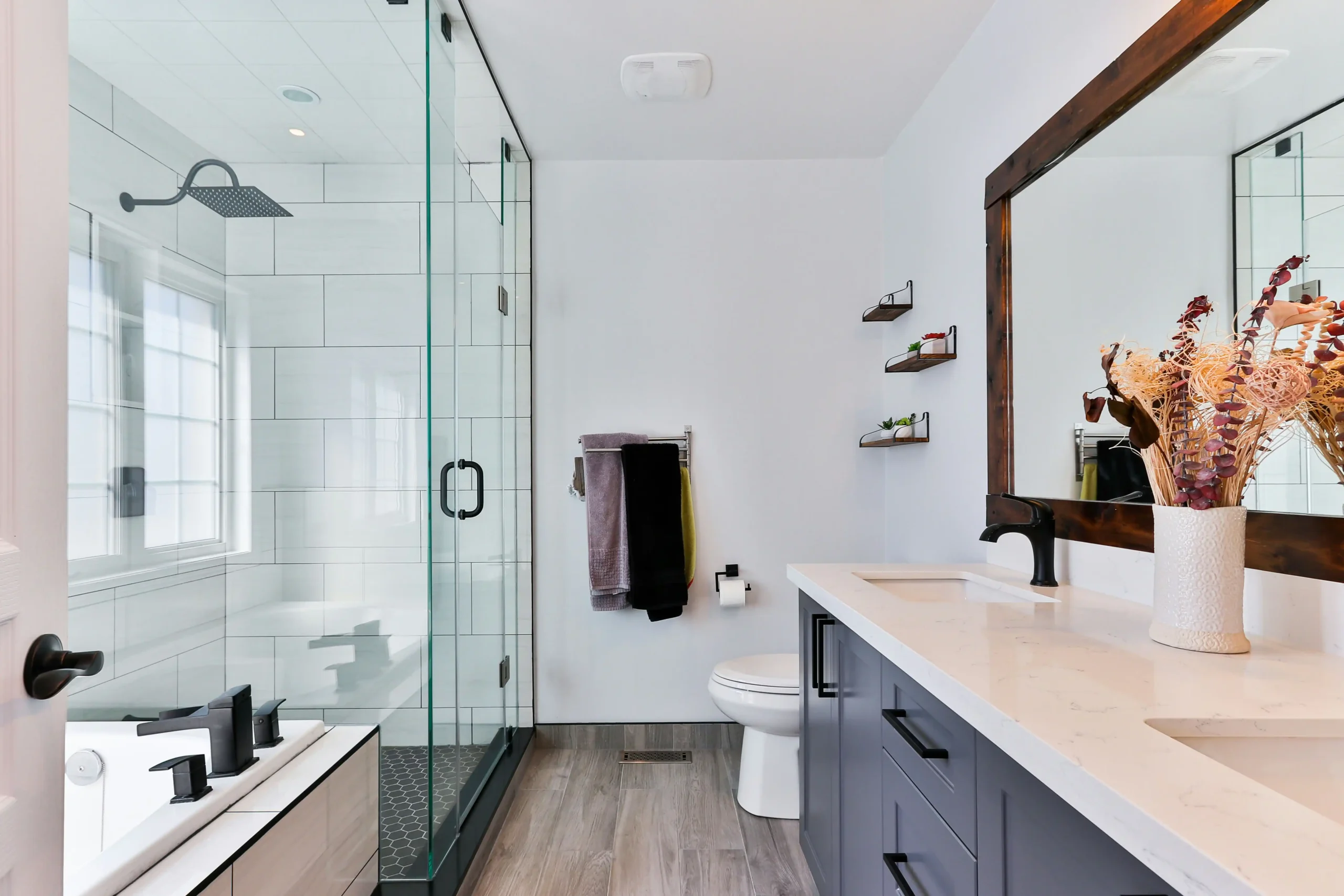 organized bathroom remodel materials staged in a garage, including labeled boxes of brass fixtures, stacked patterned tile, floating wood vanity, and frameless shower glass crate