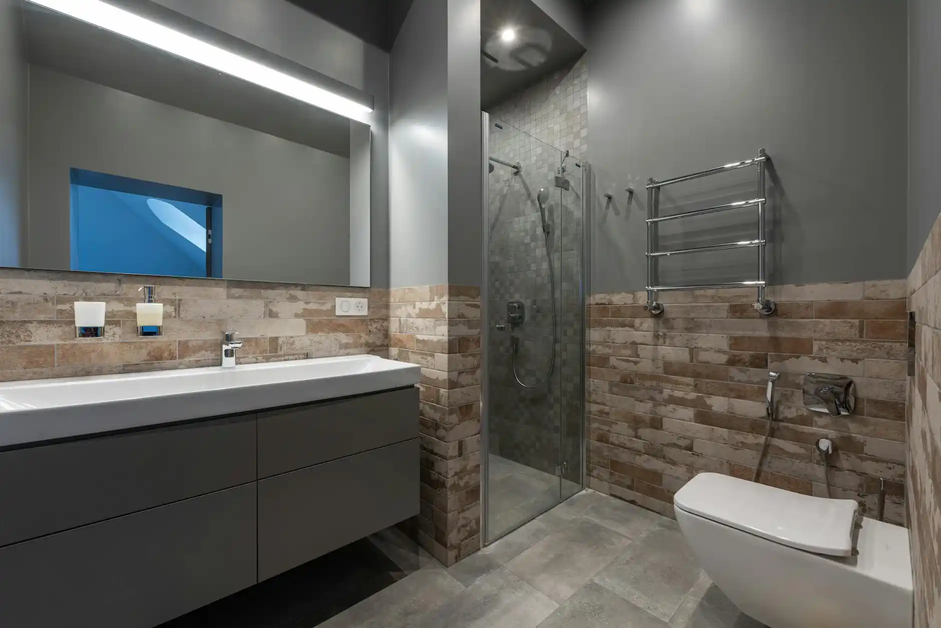elegant remodeled primary bathroom with floating oak vanity, quartz countertop, walk-in shower with frameless glass, large format porcelain tile, and warm layered lighting