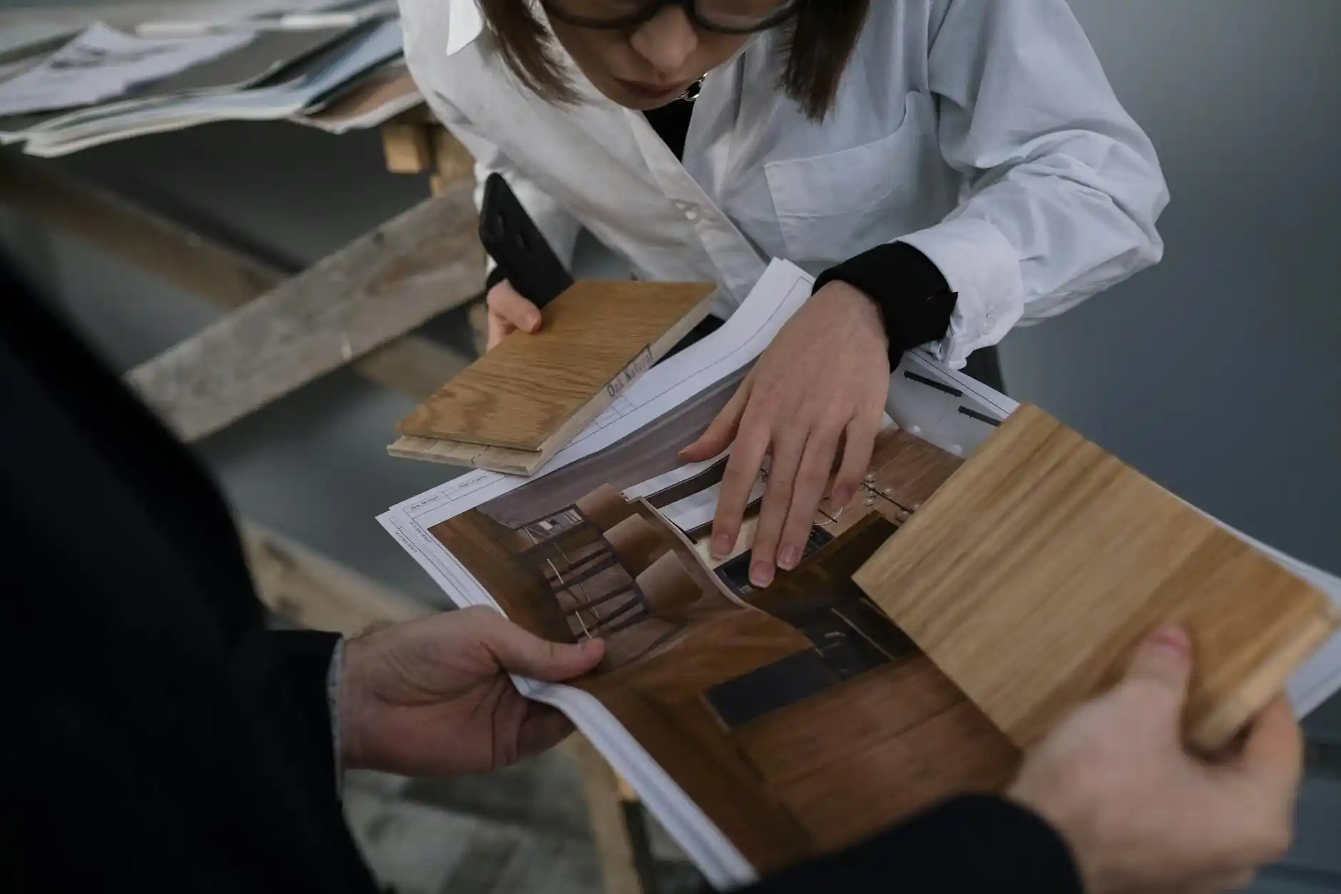 upscale custom home planning meeting with architect, builder, and homeowners reviewing blueprints on a large wood table in a bright modern office with material samples and laptops