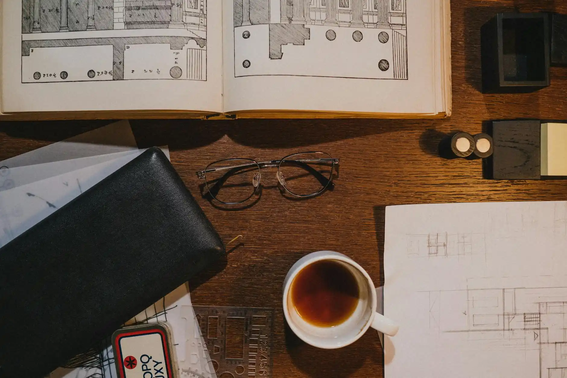 smartphone and tablet displaying residential construction schedule, progress checklist, and messaging app beside printed house plans and a cup of coffee on a clean desk