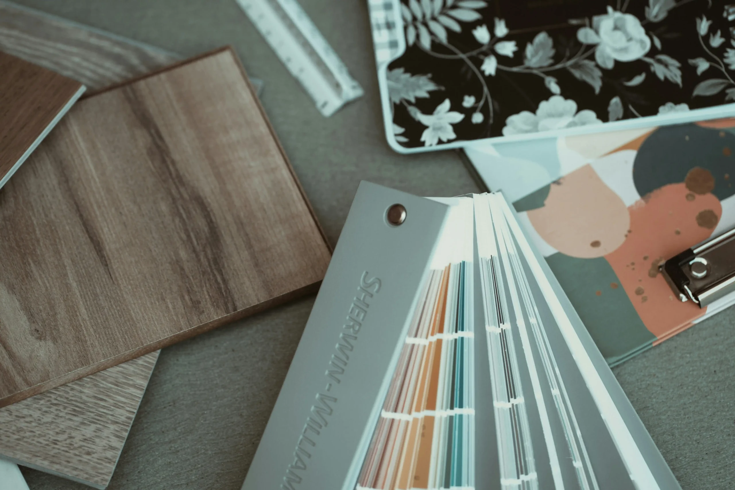 custom home consultation at a bright wood-and-glass office table, builder reviewing blueprints with a couple, material samples, coffee mugs, large windows overlooking a wooded r...