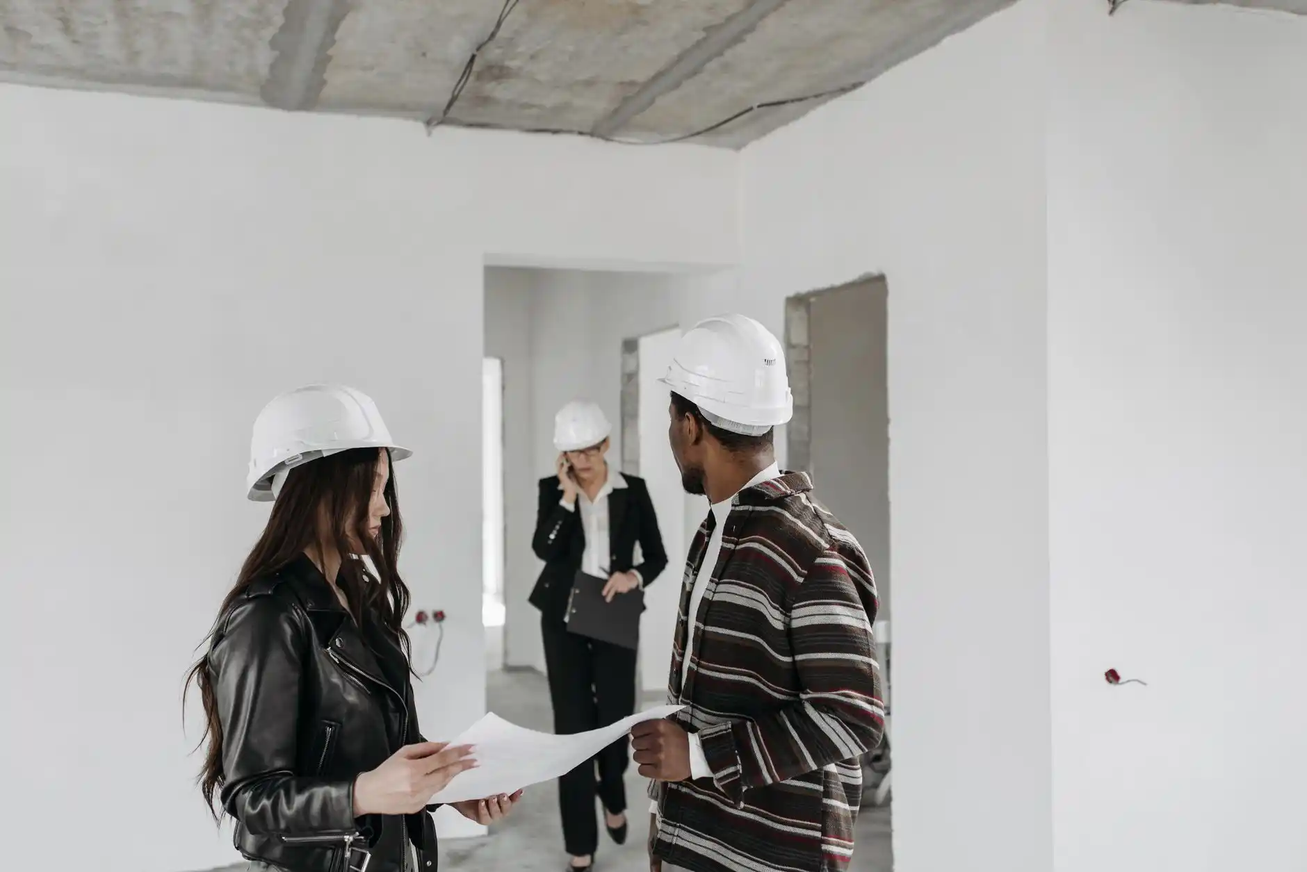 upscale custom home under construction with exposed wood framing, large steel windows, and builder and designer walking the site in hard hats at sunset