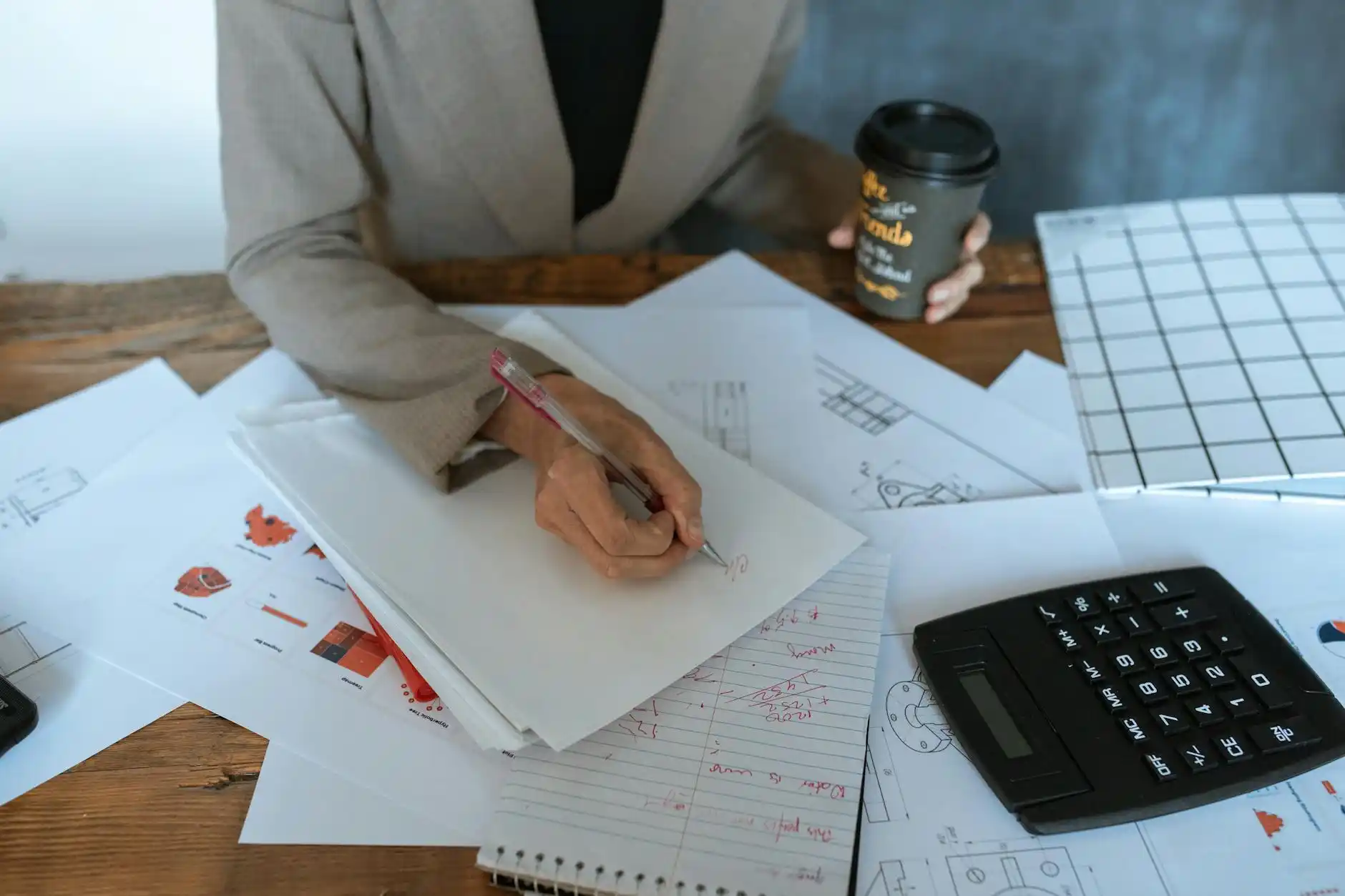 homeowner seated at a wood desk comparing financing offers on a laptop, with bathroom tile samples, printed loan documents, calculator, and coffee in natural morning light
