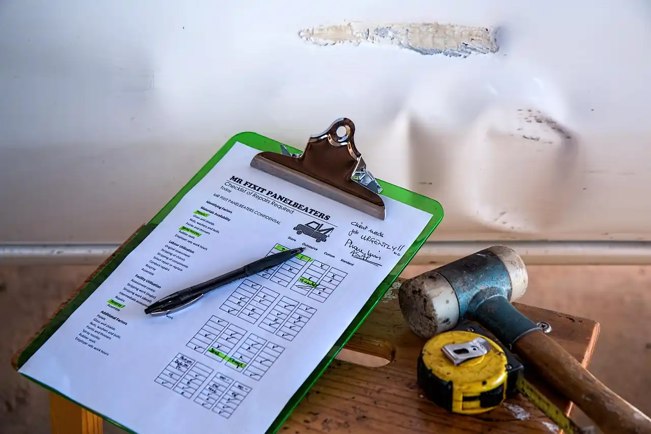 detailed construction cost estimate spread across a wooden desk with highlighted line items, kitchen renderings, permit forms, and a calculator beside tile and hardwood samples