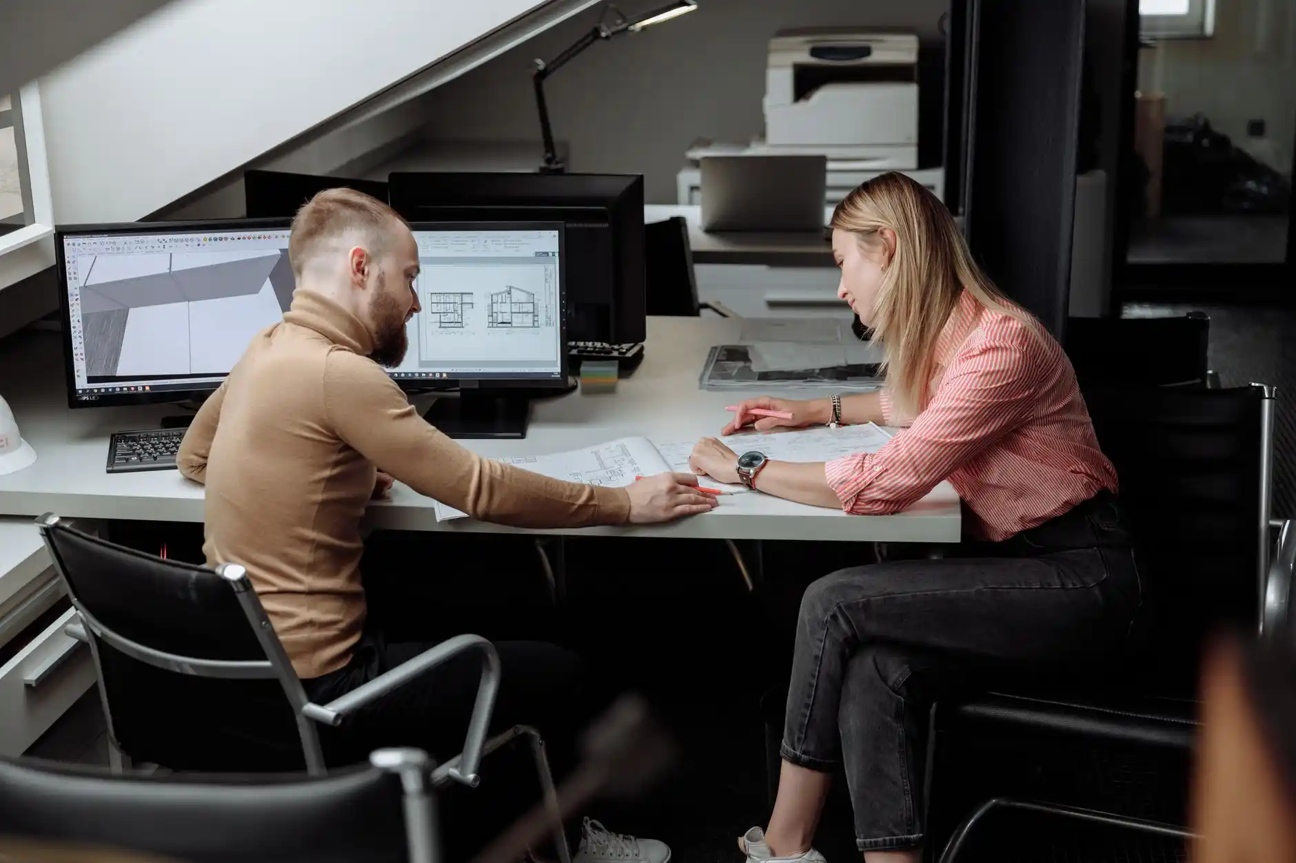 lender office meeting with borrower, contractor, and architectural plans spread across a polished wood desk, showing renovation draw schedule charts