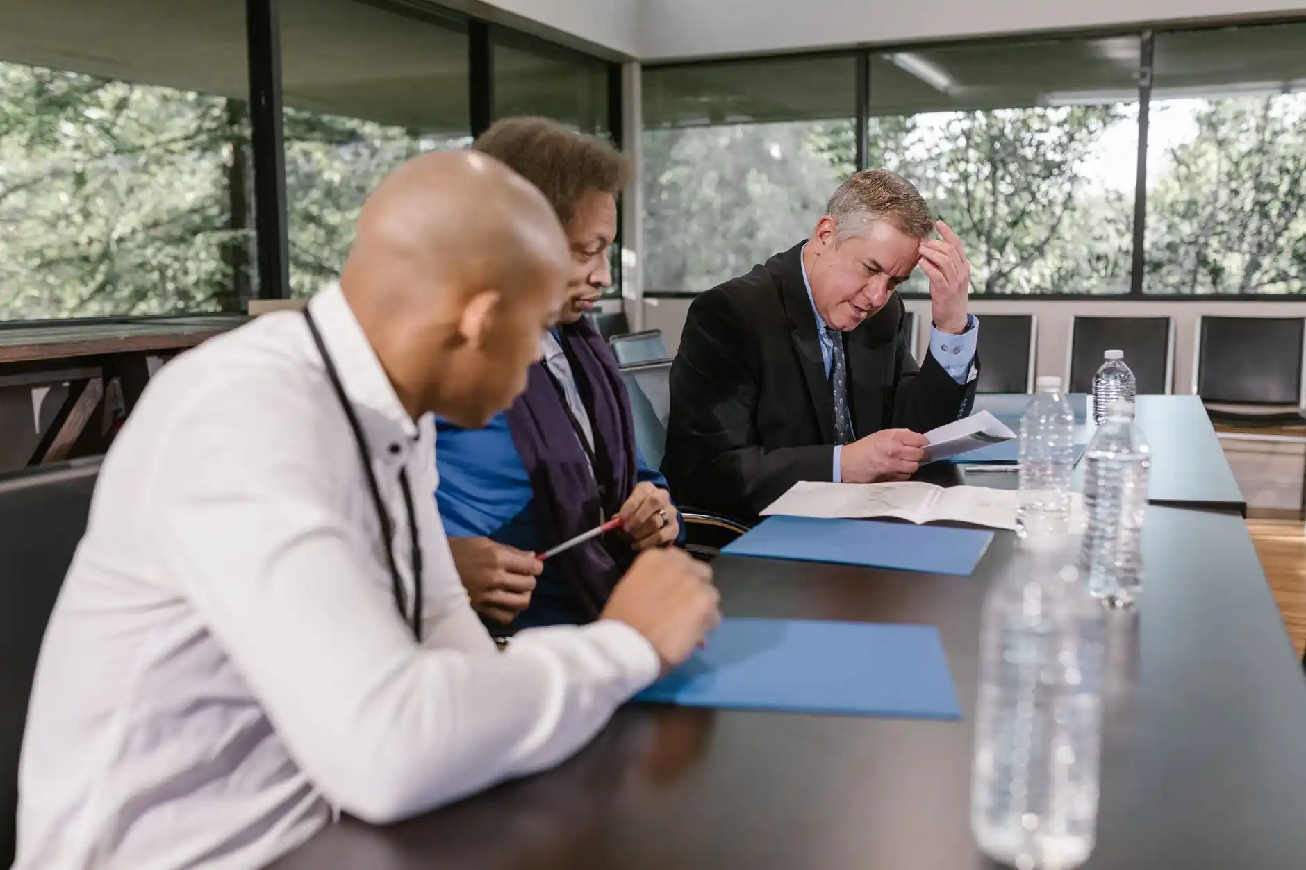 polished design-build office meeting with homeowners reviewing 3D bathroom renderings, permit documents, finish boards, and construction schedule around a wood conference table