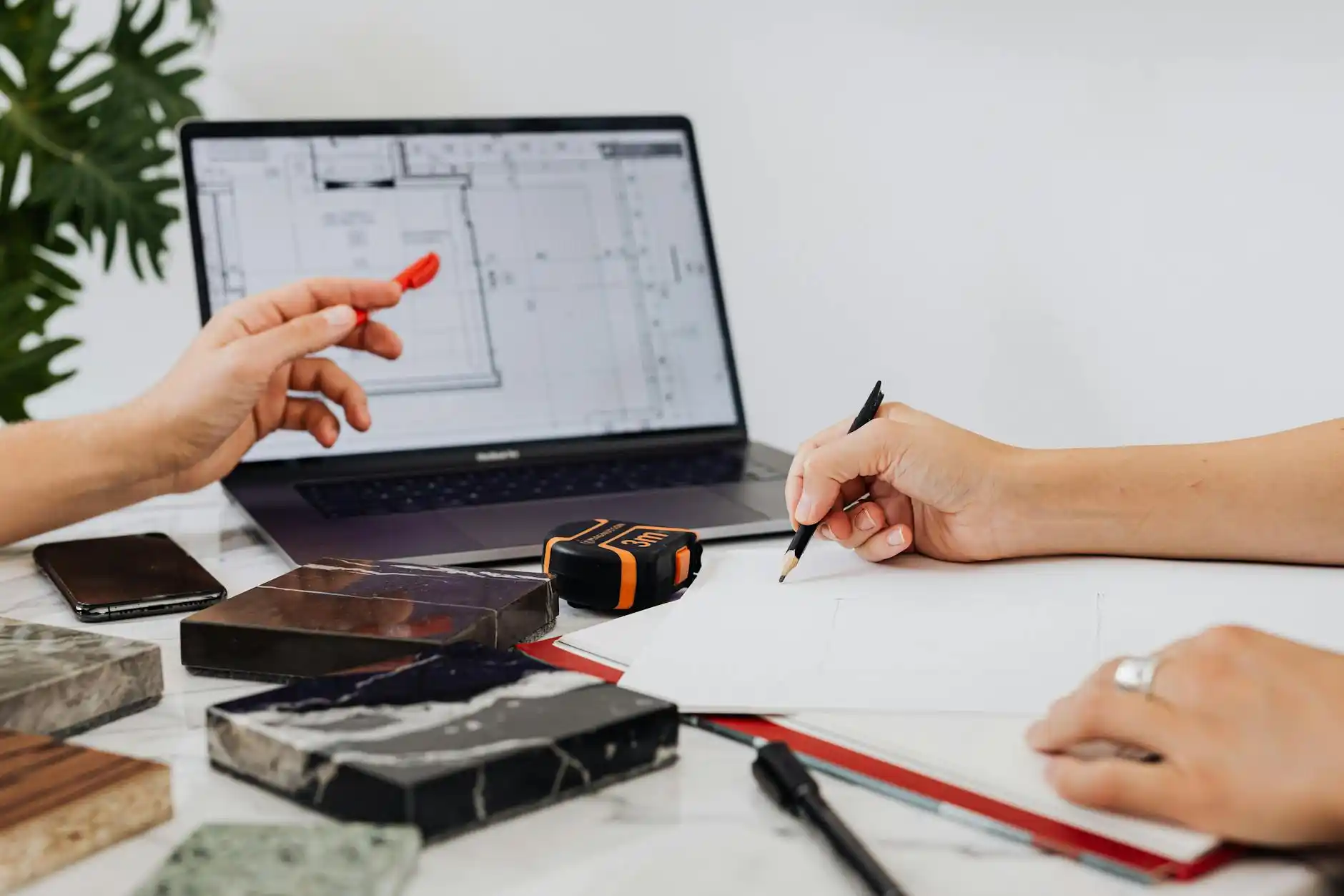 young couple reviewing home renovation plans with a mortgage advisor at a bright desk, laptop open to budget spreadsheet, suburban fixer-upper photo boards in the background