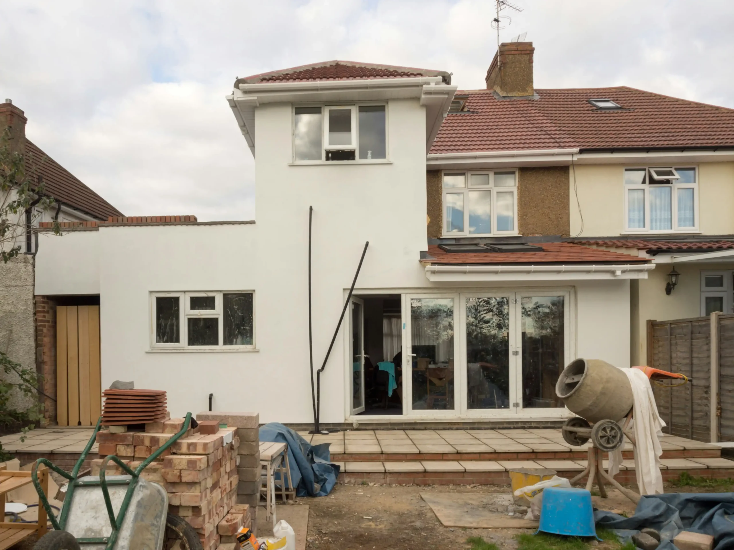 split-view of a house showing minor cosmetic updates on one side and major structural renovation with exposed framing and new layout plans on the other