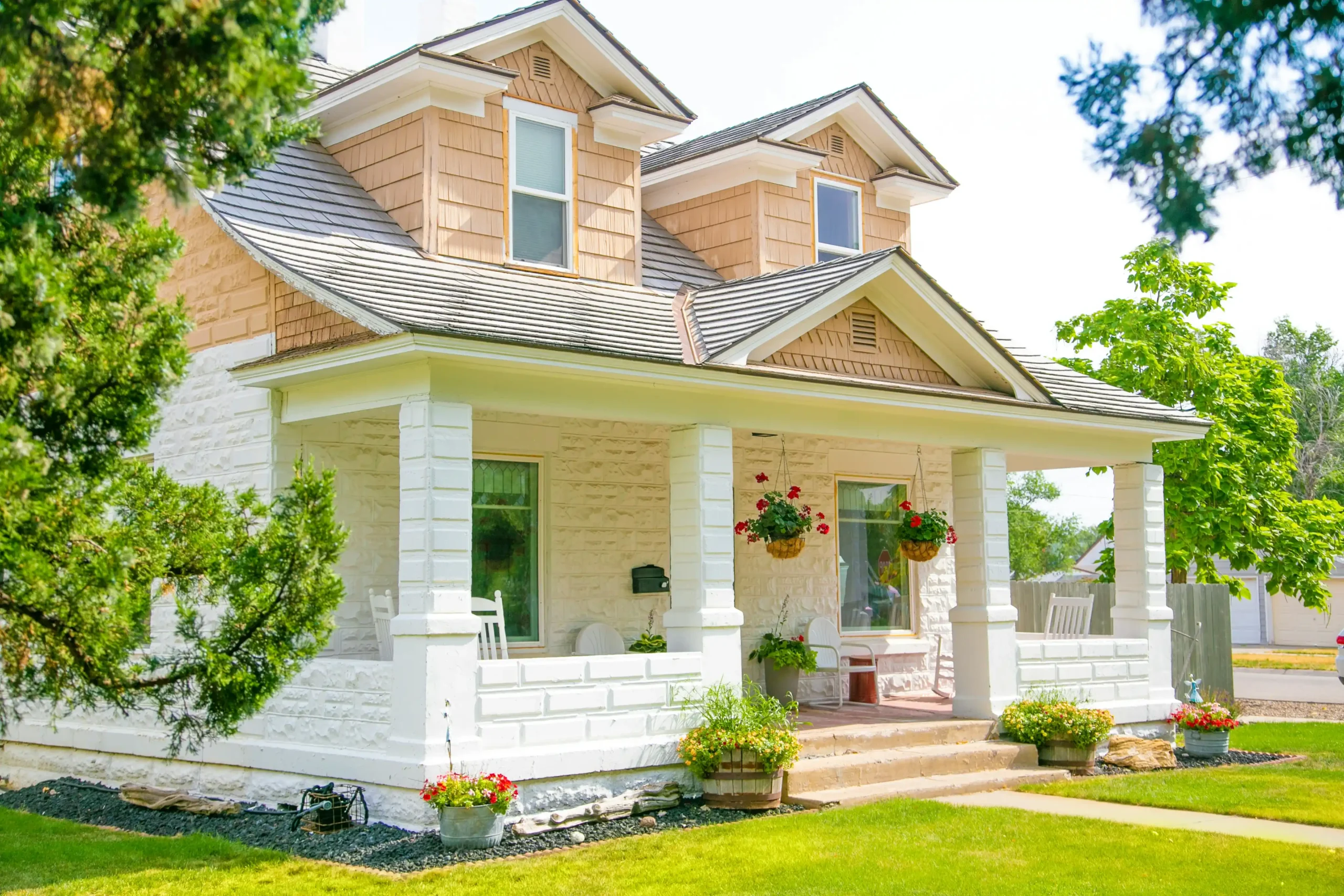 bright, well-prepared suburban home exterior with fresh mulch, trimmed shrubs, clean walkway, painted front door, and a real estate photographer setting up a camera at golden hour