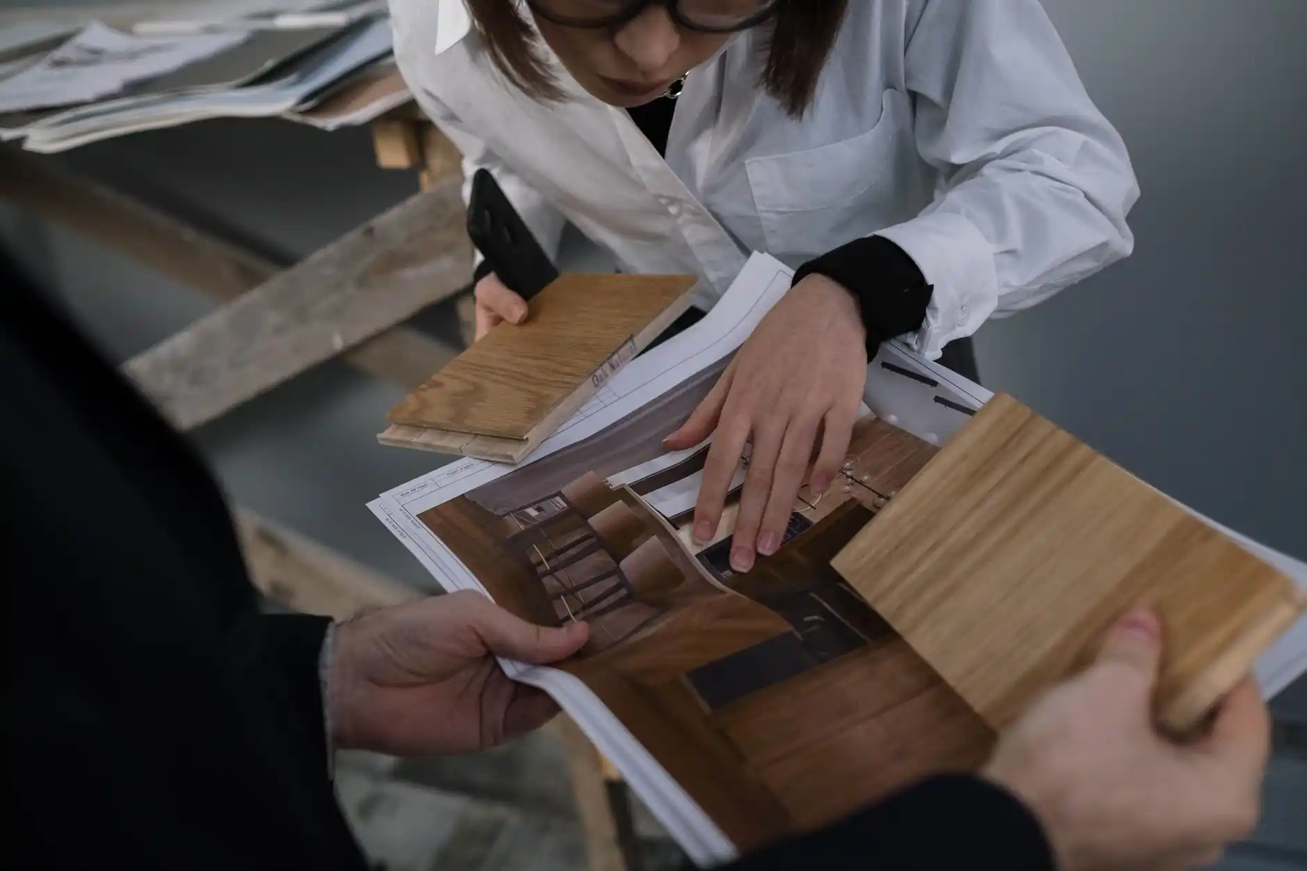 Photorealistic homeowner interview with a remodeling firm, showing a contract, project schedule, insurance certificate, material samples, and tablet displaying completed renovat...